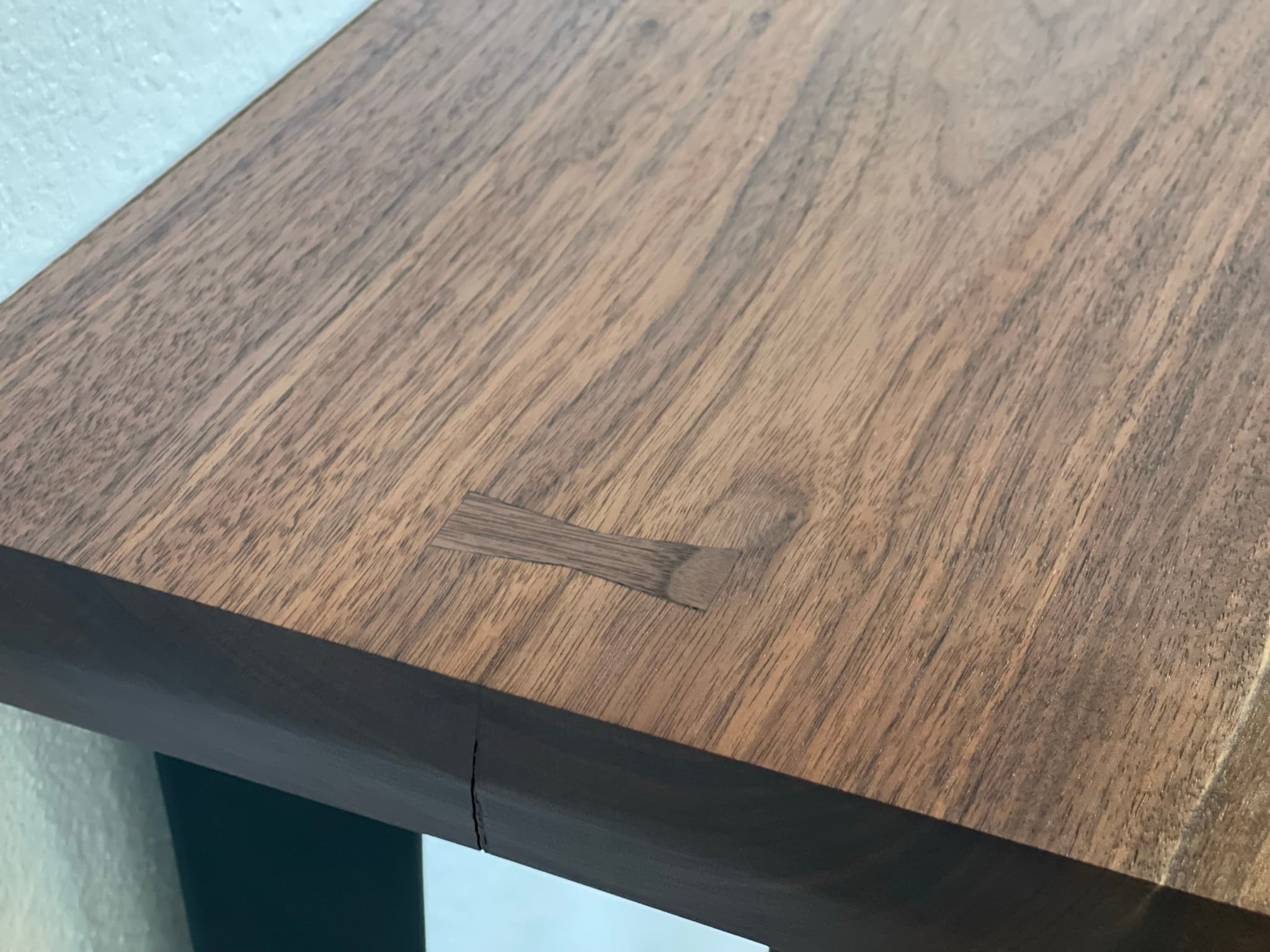Top-down close-up of a contrasting bowtie inlay set across a small check in the walnut top, grain running diagonally across the frame.