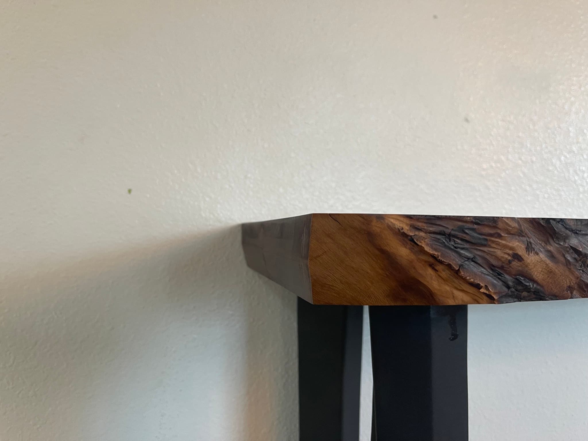 End-of-slab close-up: the chamfered end-grain cut on the left, the burr live edge running back to the right, with one blackened steel leg visible underneath.
