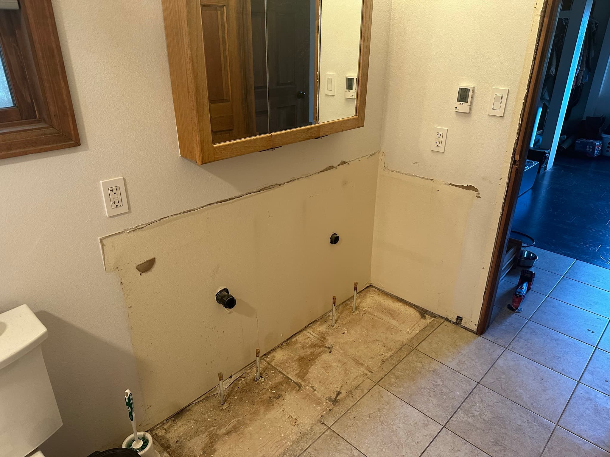Vanity removed: drain stub and supply lines sticking up from the floor where the cabinet sat, drywall cut back around the old footprint.