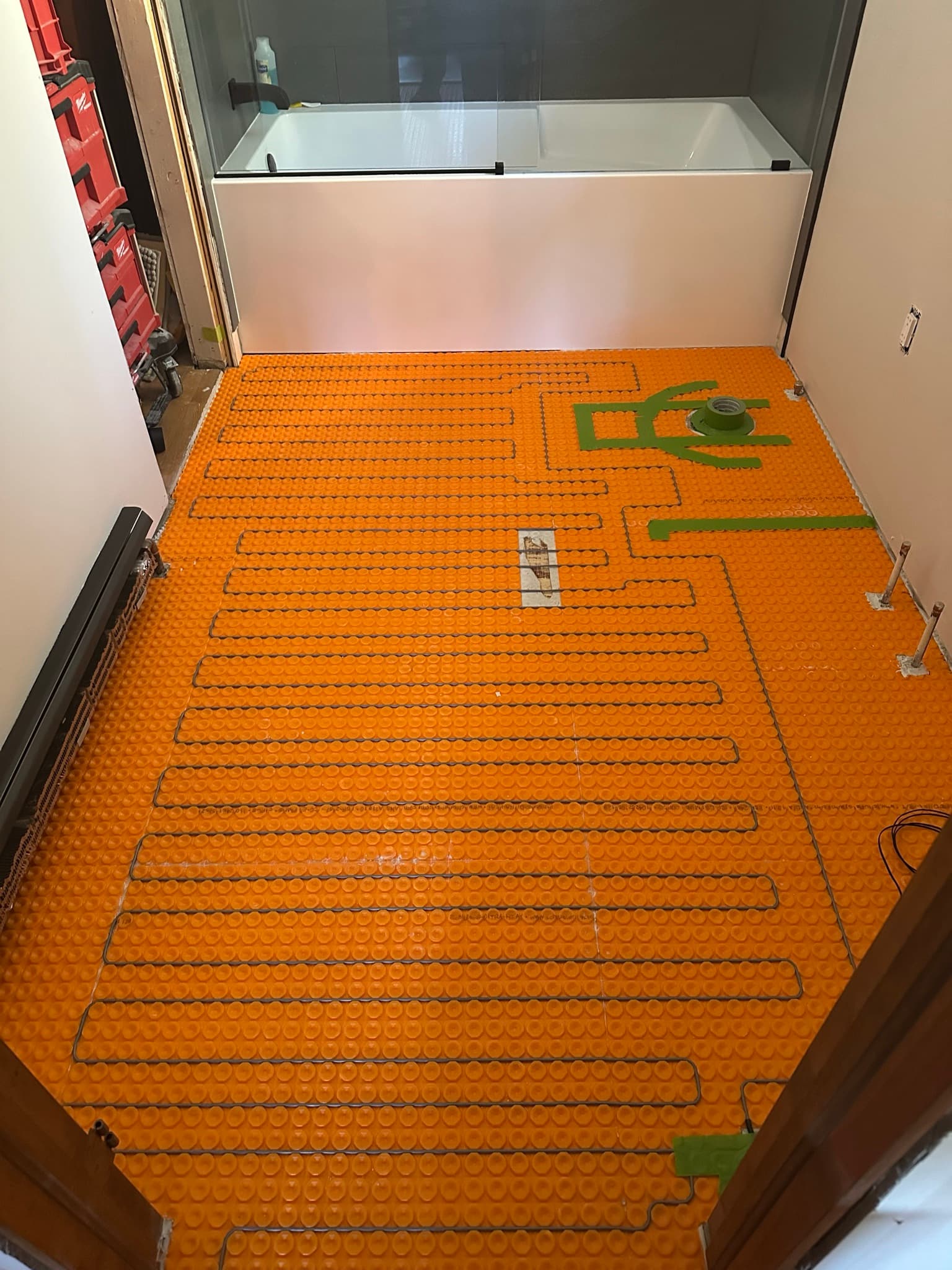 Heated-floor cable run in a tight serpentine across the Ditra-Heat membrane on the bathroom floor, with a thermostat sensor terminating in a marked area.