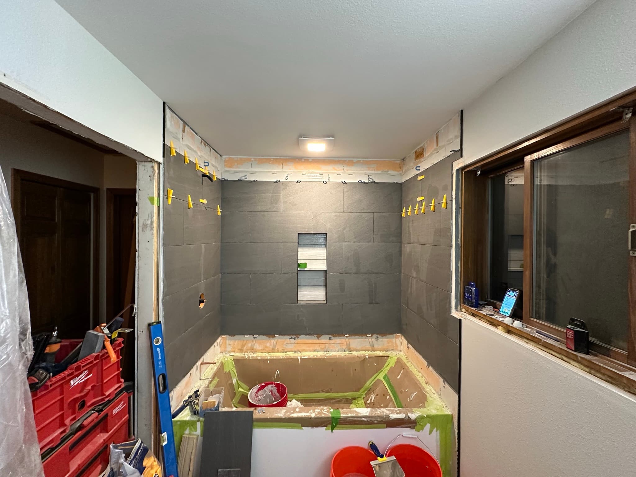 Three walls of tub surround tiled, top row of leveling clips still in place near the ceiling, niche visible center-back.