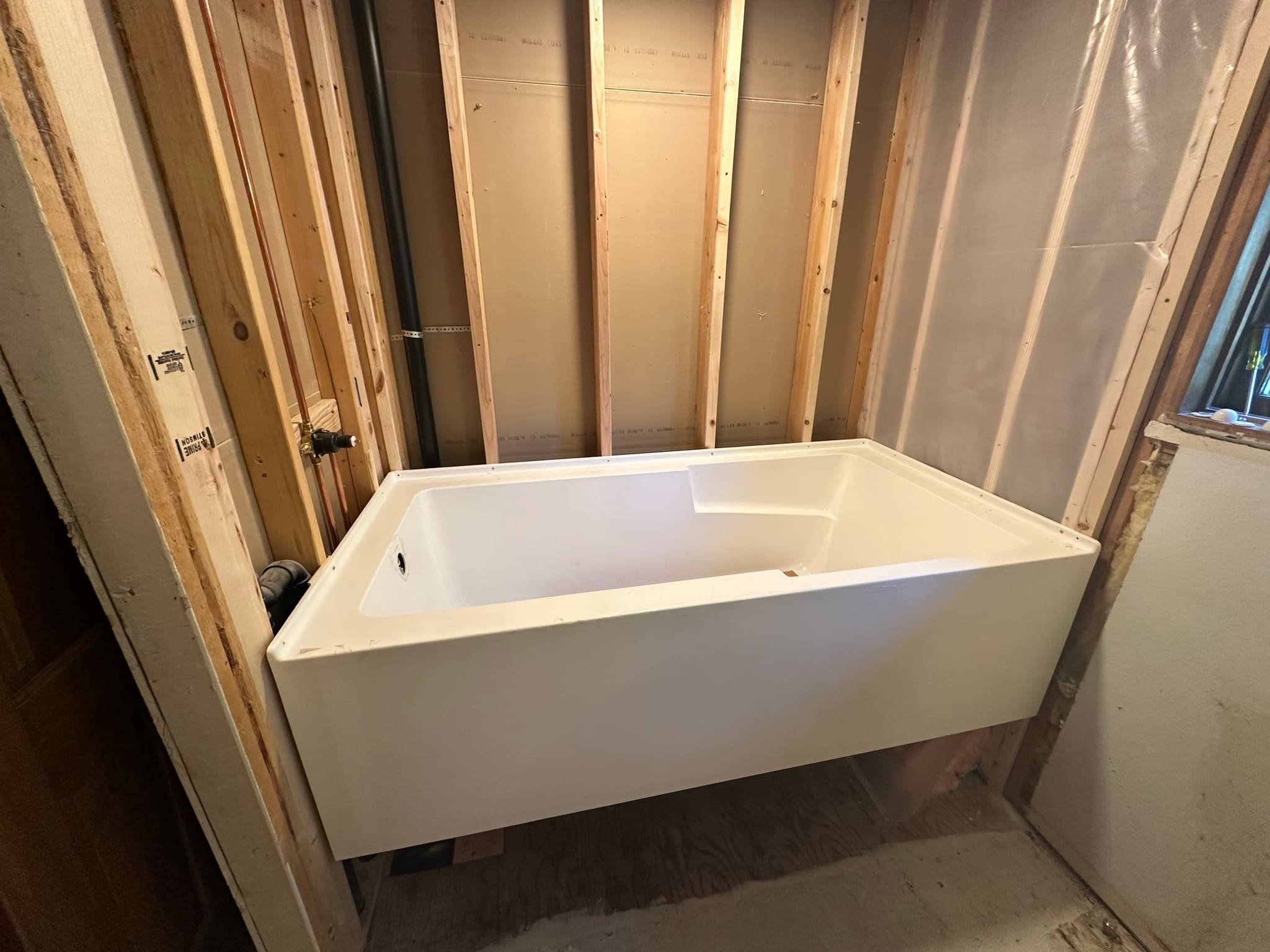 Alternate angle of the same alcove tub install, shower valve rough visible at left, no surround yet.