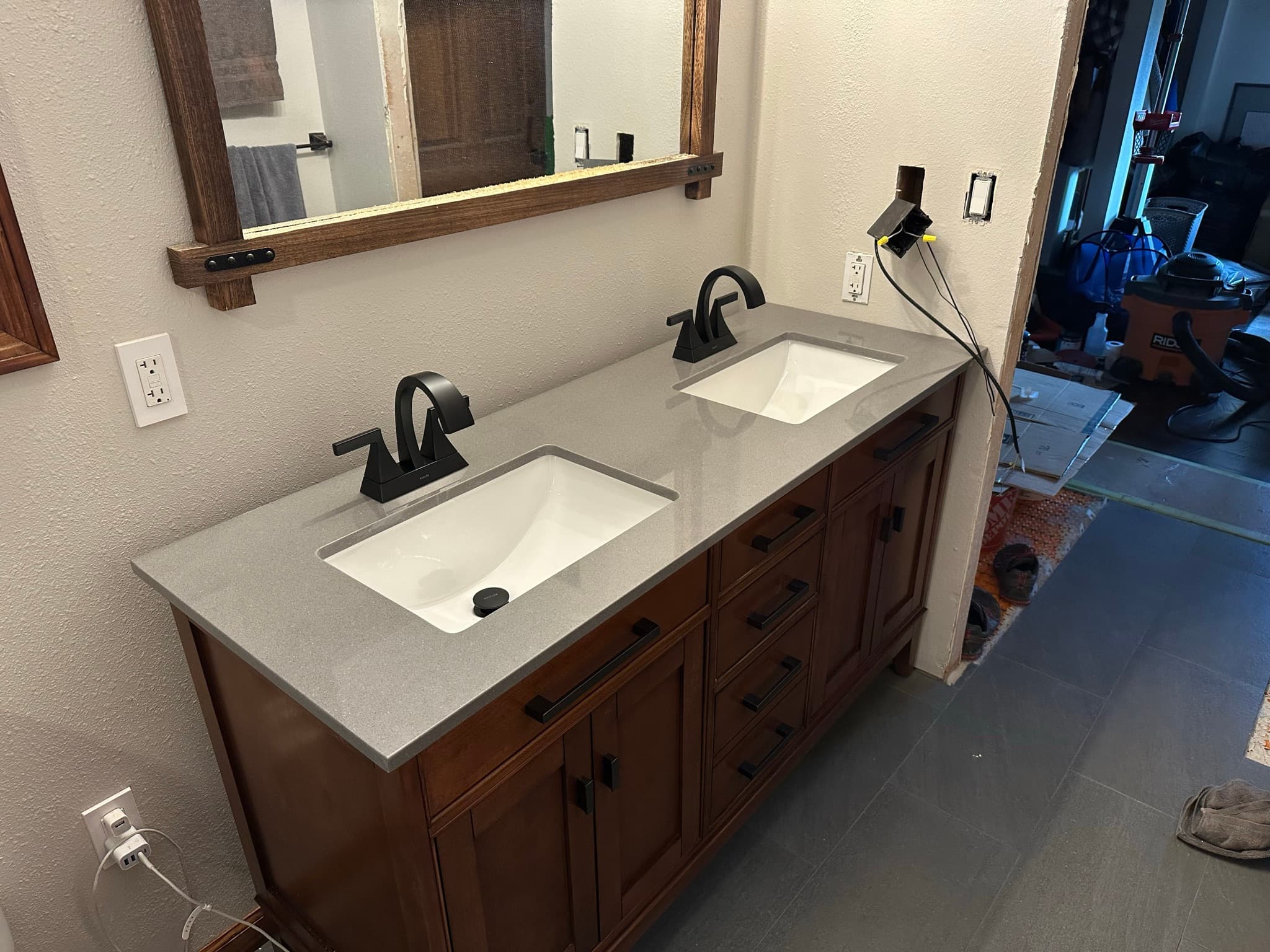Vanity with gray quartz countertop installed: two rectangular undermount sinks, matte-black faucets, light fixture being wired at the right.