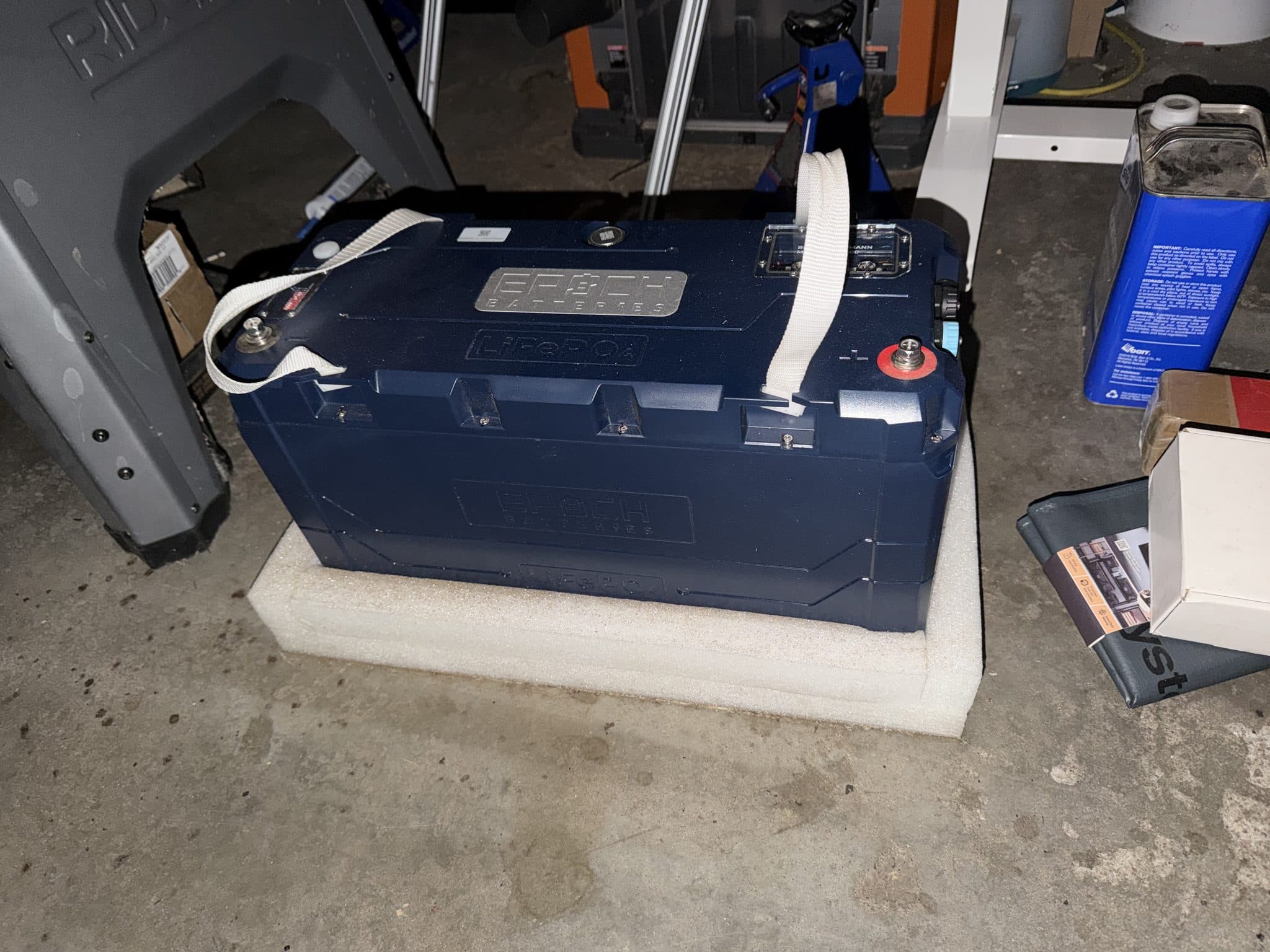 Epoch Batteries LiFePO4 house battery resting on foam padding in the garage before installation, lifting straps still attached.