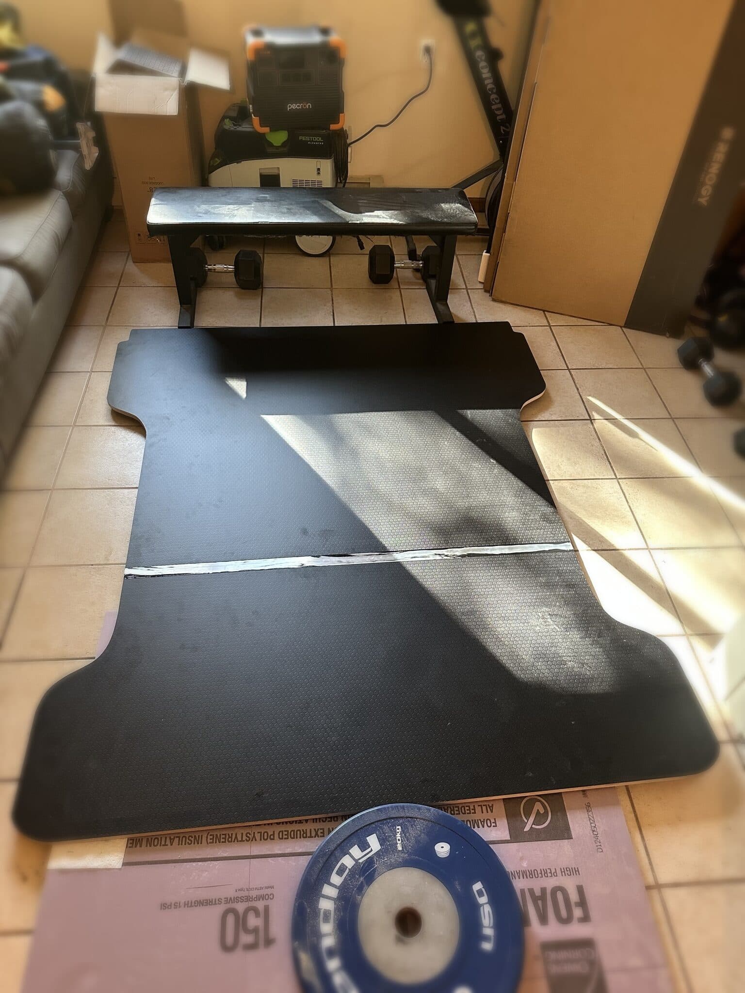 The two-piece deck panel joined at a glue seam, laid flat on a living room tile floor over foam insulation board with a 20-kilogram bumper plate weighting the joint.