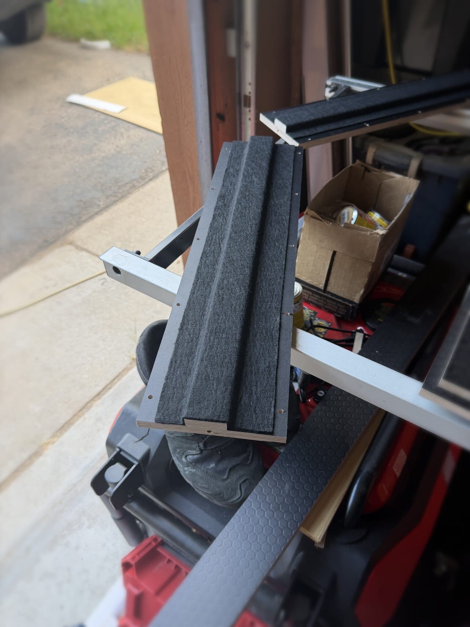 Plywood rail piece with felt-lined channels resting across the garage doorway, drilled for mounting screws.