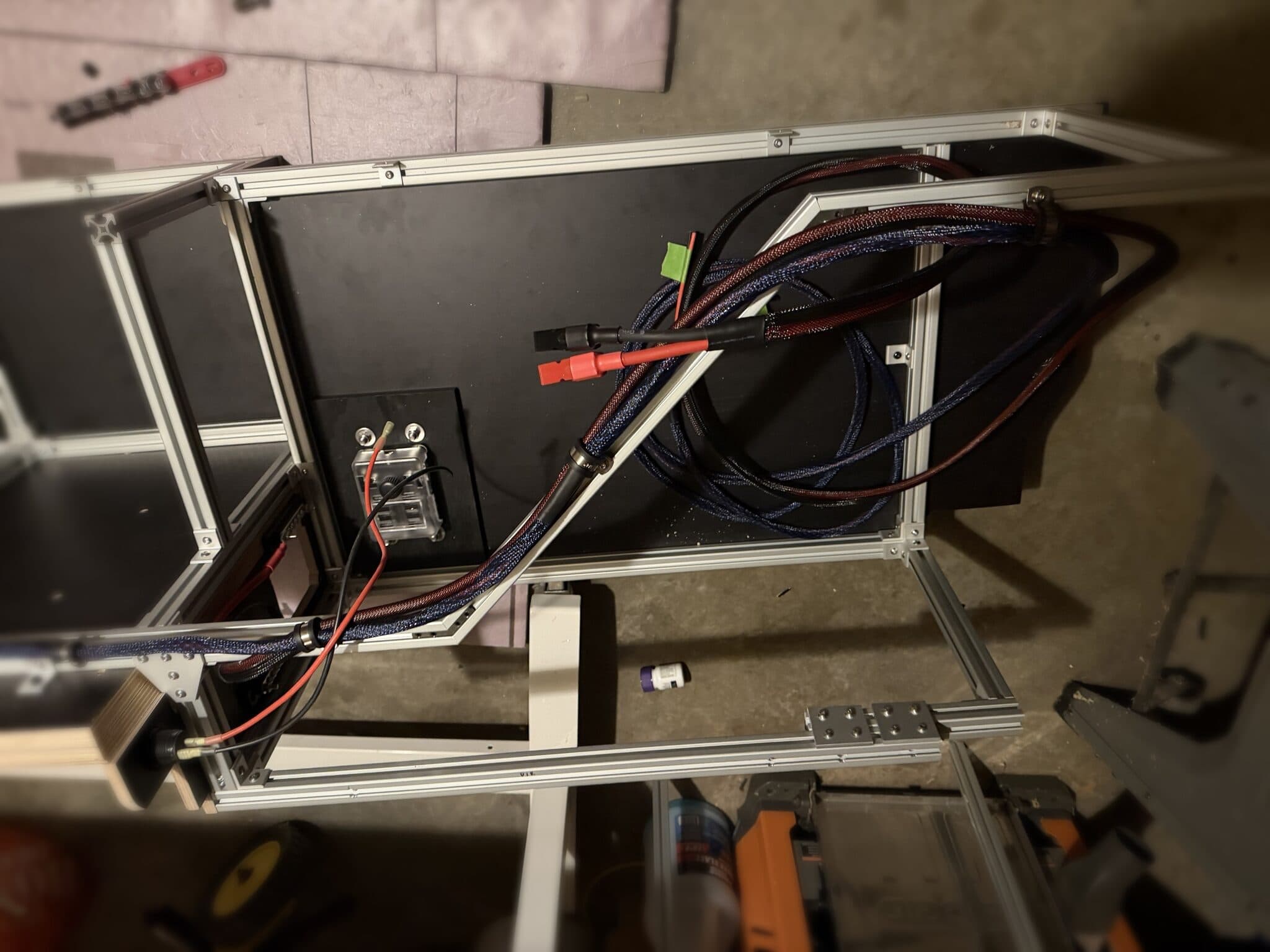Module frame on the garage floor with sleeved power cables terminated in Anderson-style connectors, routed through strain-relief glands to a 12-volt outlet panel.