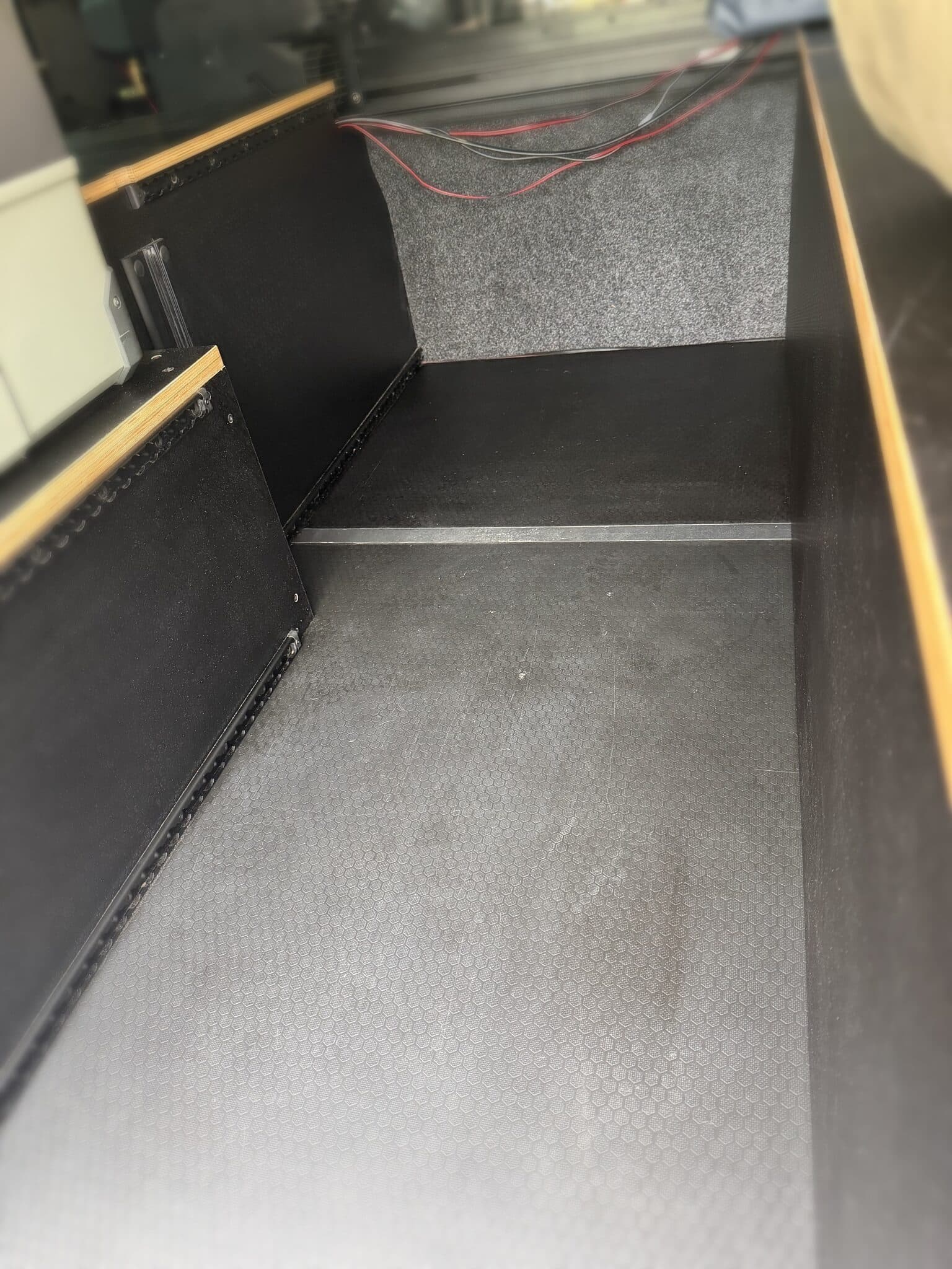 Finished storage bay inside the camper: hex-laminate floor and side panels with carpeted walls and wiring waiting at the back corner.