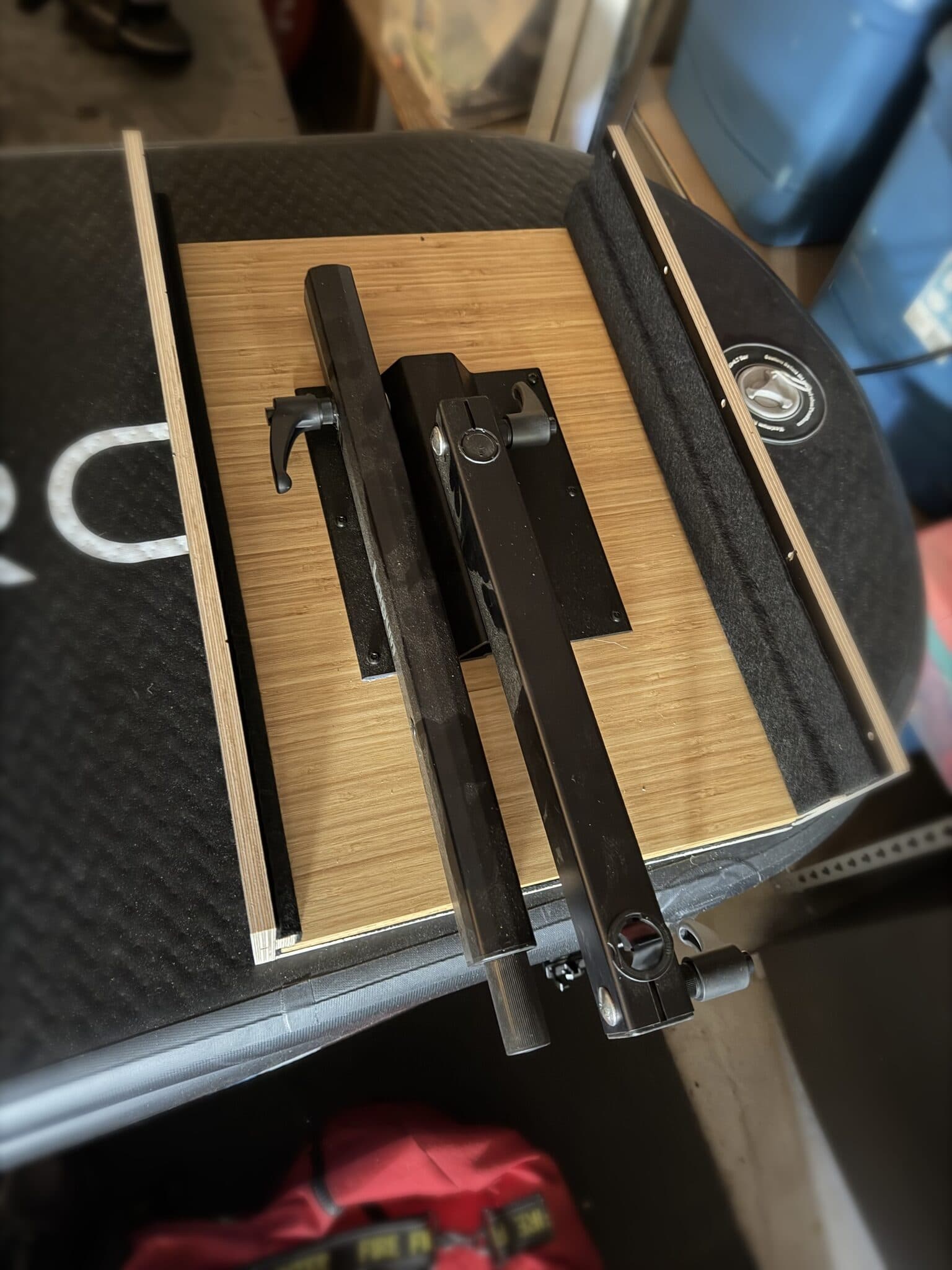 Lagun swing-arm table mount hardware laid out on a bamboo mounting board between two felt-lined plywood rails.
