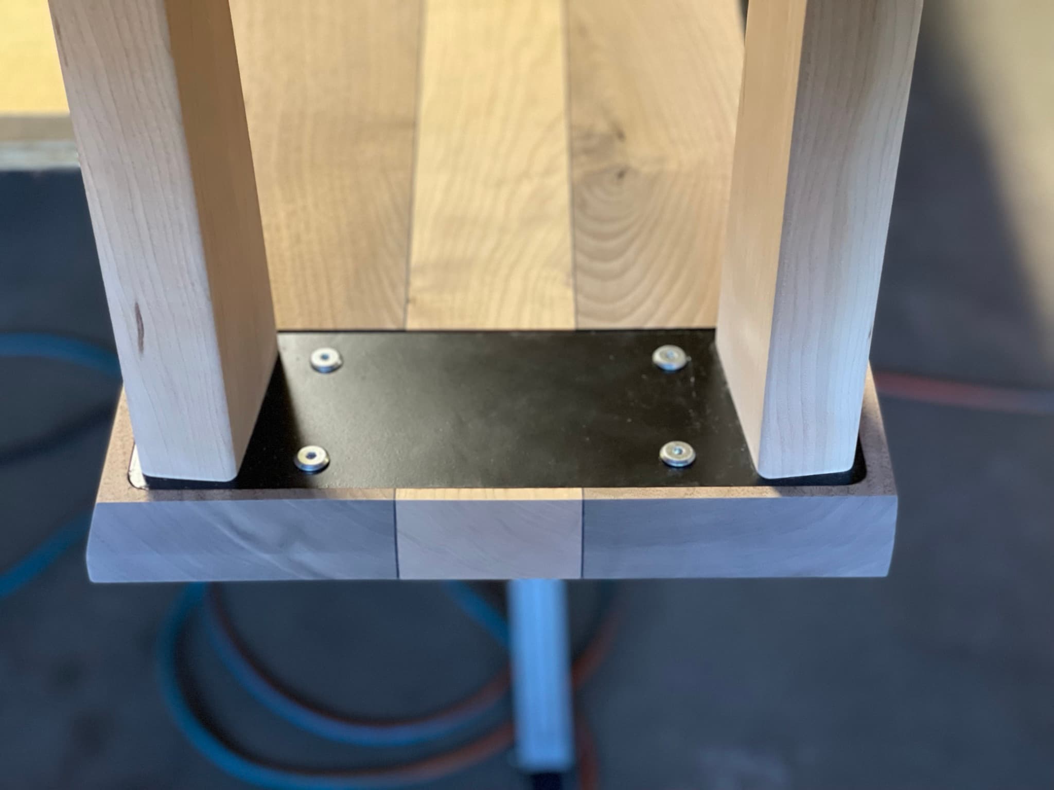 View looking up into the underside of the assembled console: four maple legs in their wells around the recessed blackened-steel structural plate.