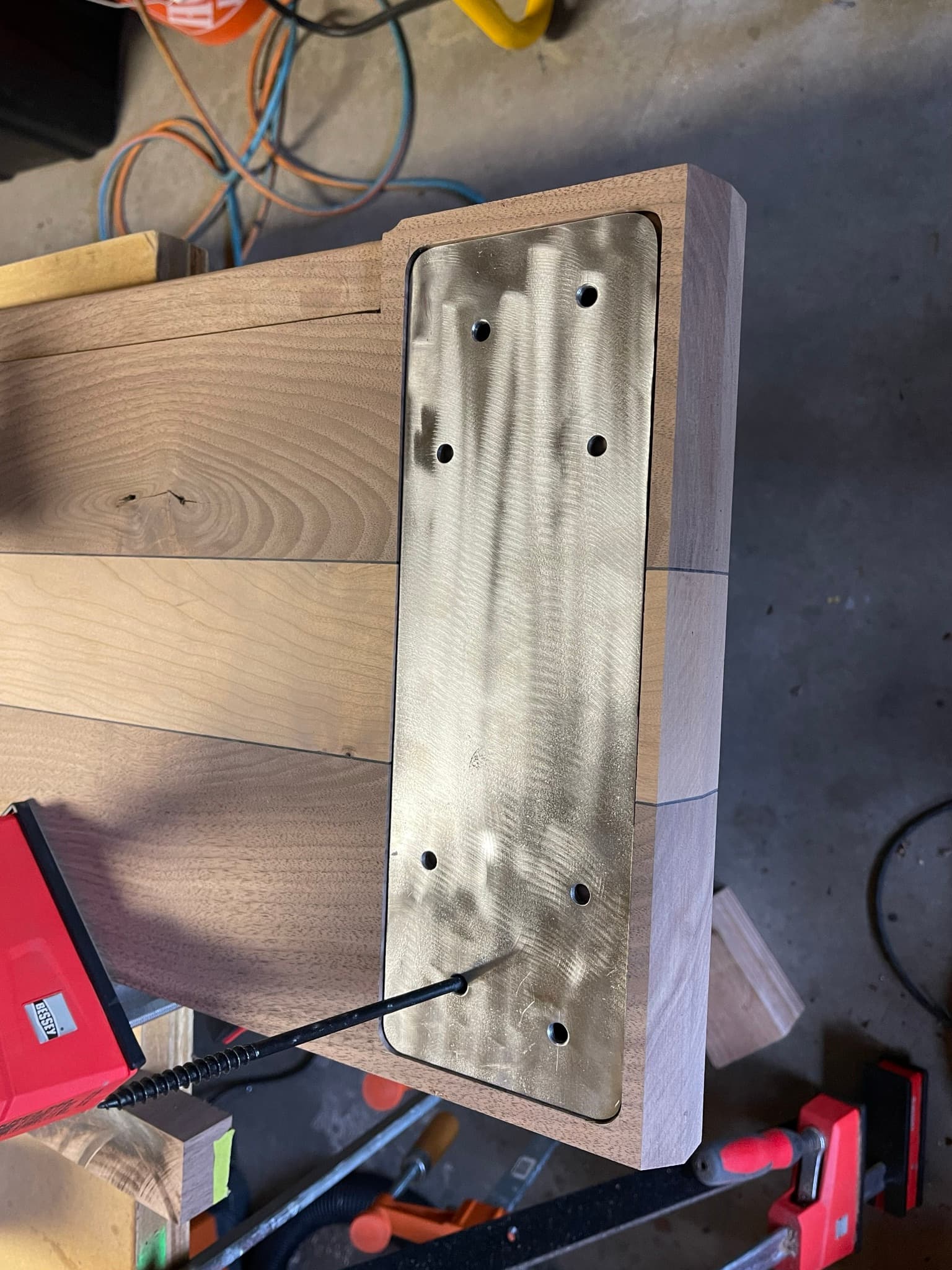 A rectangular brass plate inset flush into the underside of the maple-walnut top, with eight countersunk fastener holes.