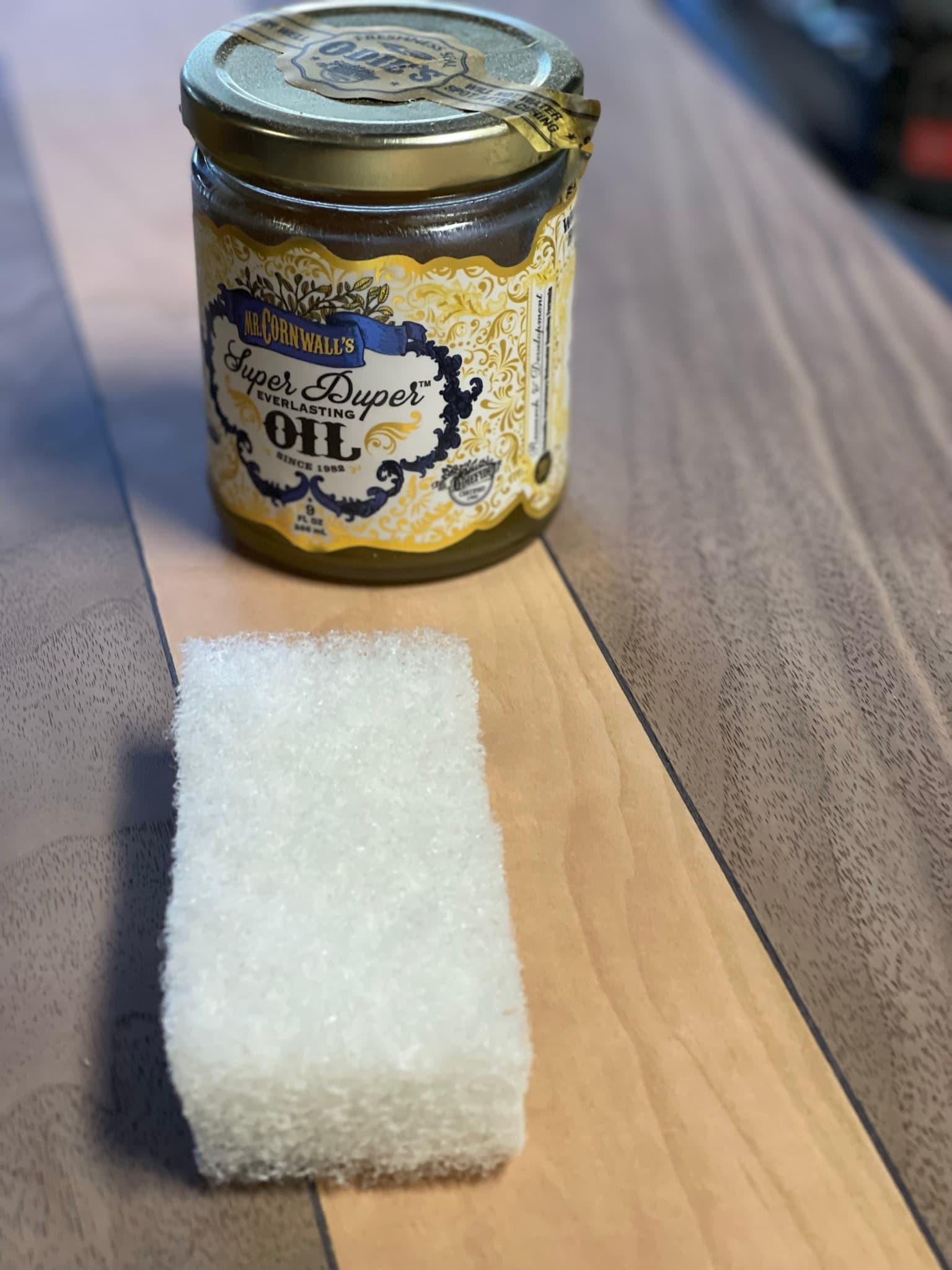 A jar of Odie's Super Duper Oil and a white scrub pad sitting on the maple field of the top before the first coat goes on.