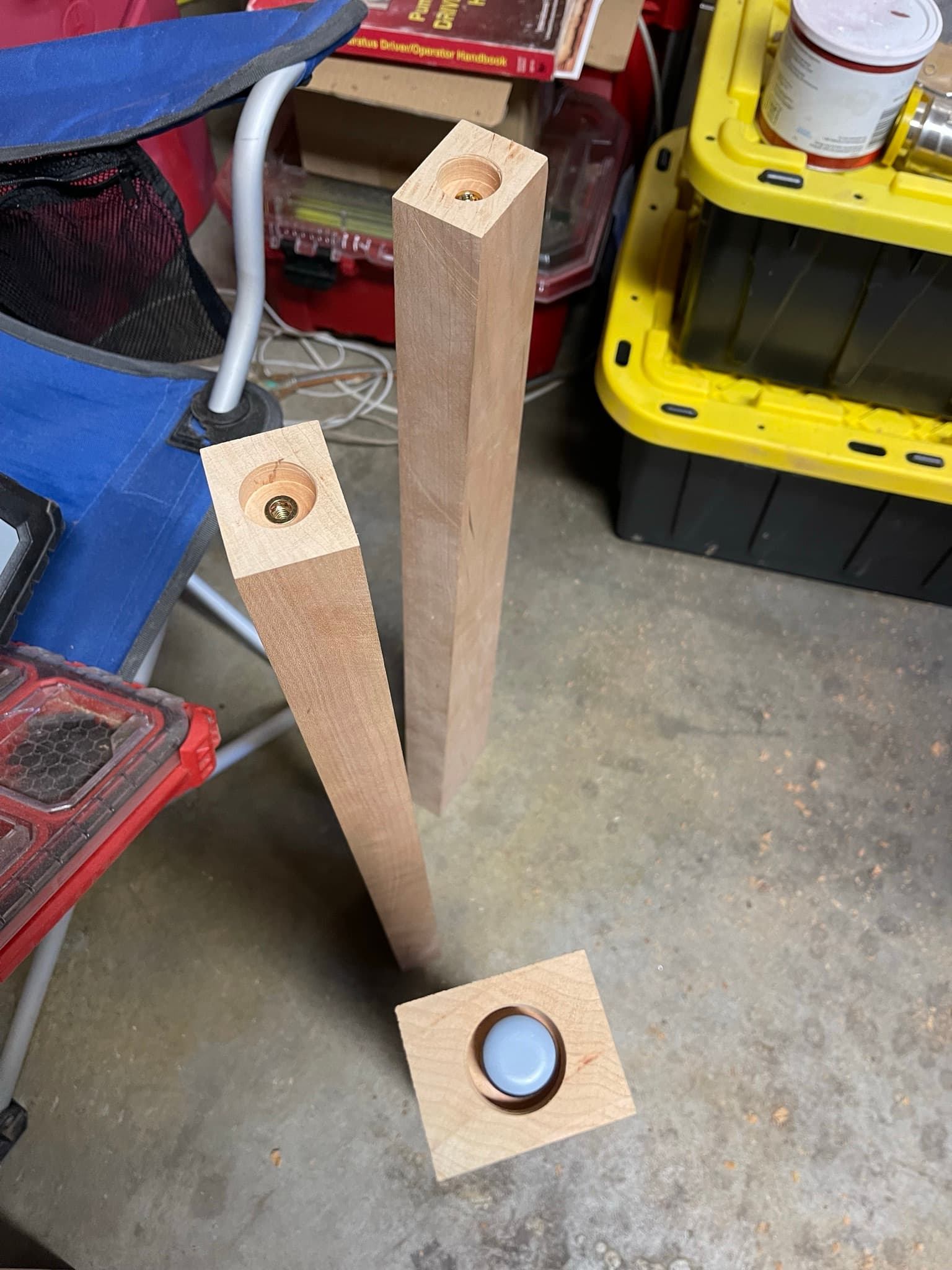 Three tapered maple legs laid on the shop floor before installation; two show the threaded inserts at the top, one shows a felt glide at the foot.